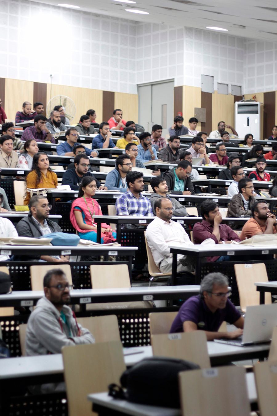 Large diverse audience seated in a tiered lecture hall, attentively listening to a presentation at PyConf Hyderabad. Attendees are focused forward with some using laptops and taking notes.