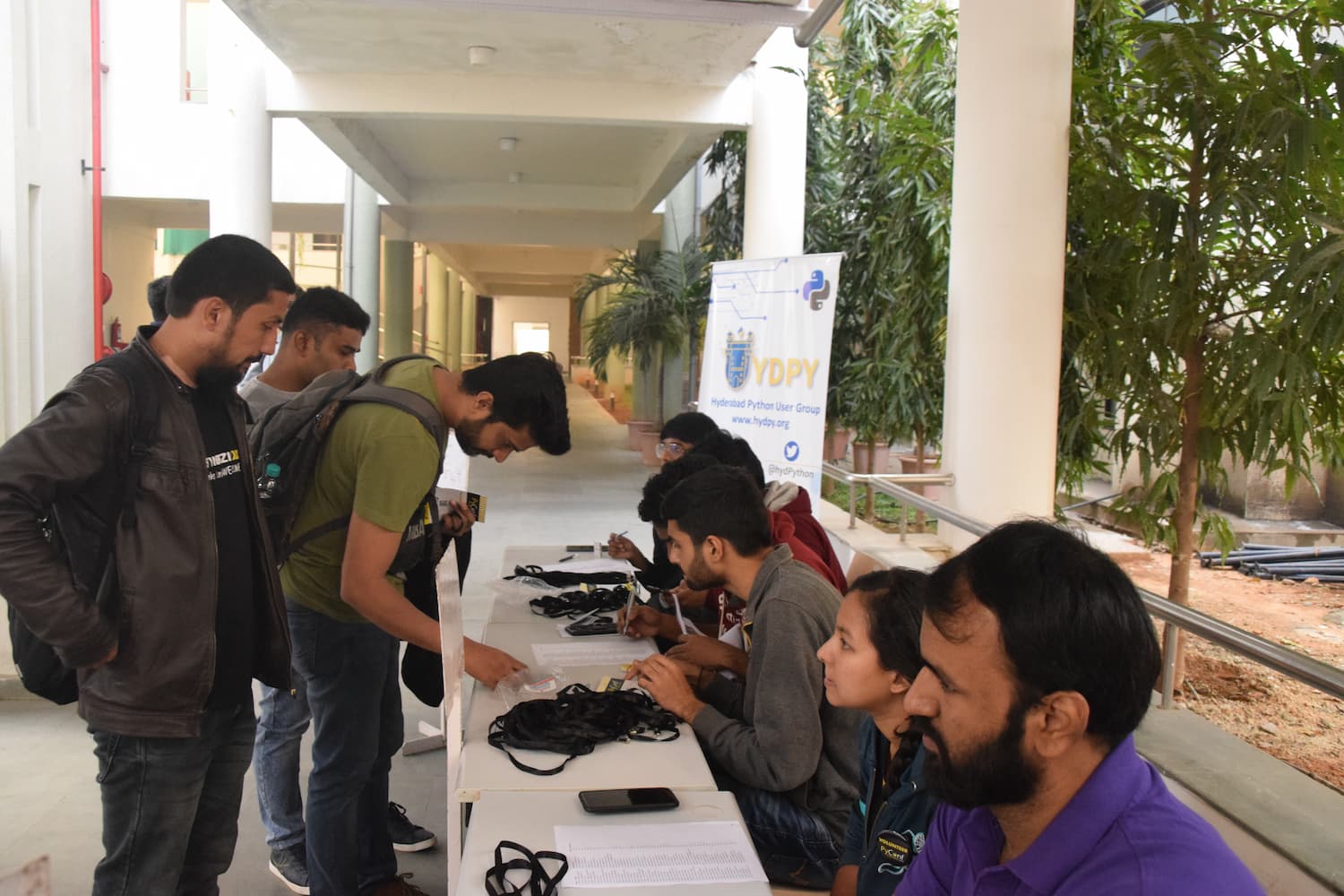 Outdoor registration desk for Hyderabad Python User Group event. Attendees and organizers gather around a table with the YDPY banner visible, featuring the Python logo and www.hydpy.org.