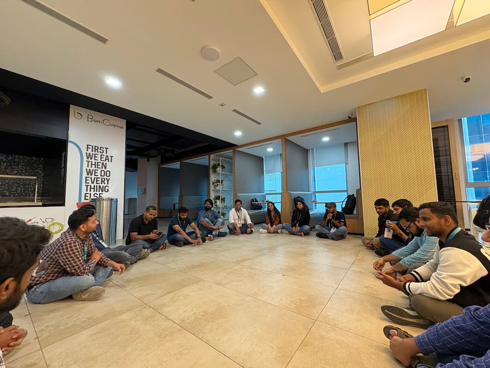 Informal gathering of attendees sitting in a circle on the floor, engaged in discussion at a modern event space with Bon-Cuisine banner visible in the background.